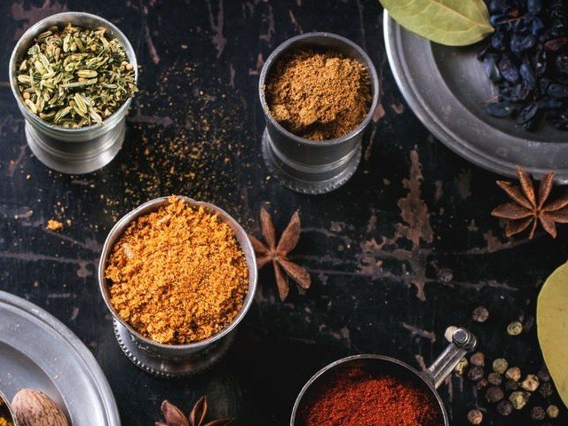 Venkelzaad, garam masala en kurkuma in metalen bekertjes, met steranijs en peperkorrels op een donkere tafel.